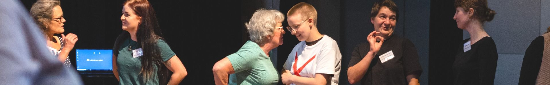 Menschen stehen zu Zweiergruppen zusammen und unterhalten sich. Das Gesicht ist dem:der jeweiligen Gesprächspartner:in zugewandt.