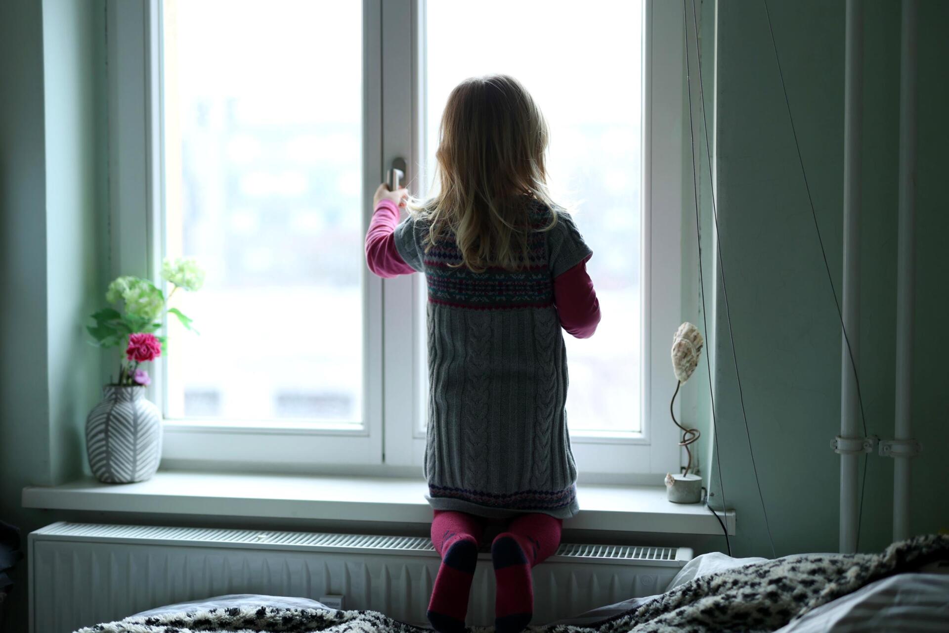 kleines Mädchen am Fenster mit Hand am Fenstergriff Gefahr