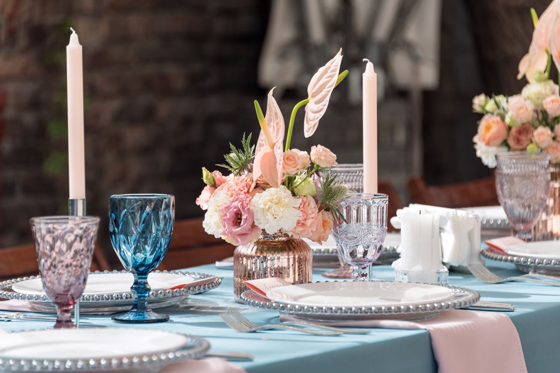 Table nappée bleue avec verres à pieds colorés et centre de table fleuri - wedding design