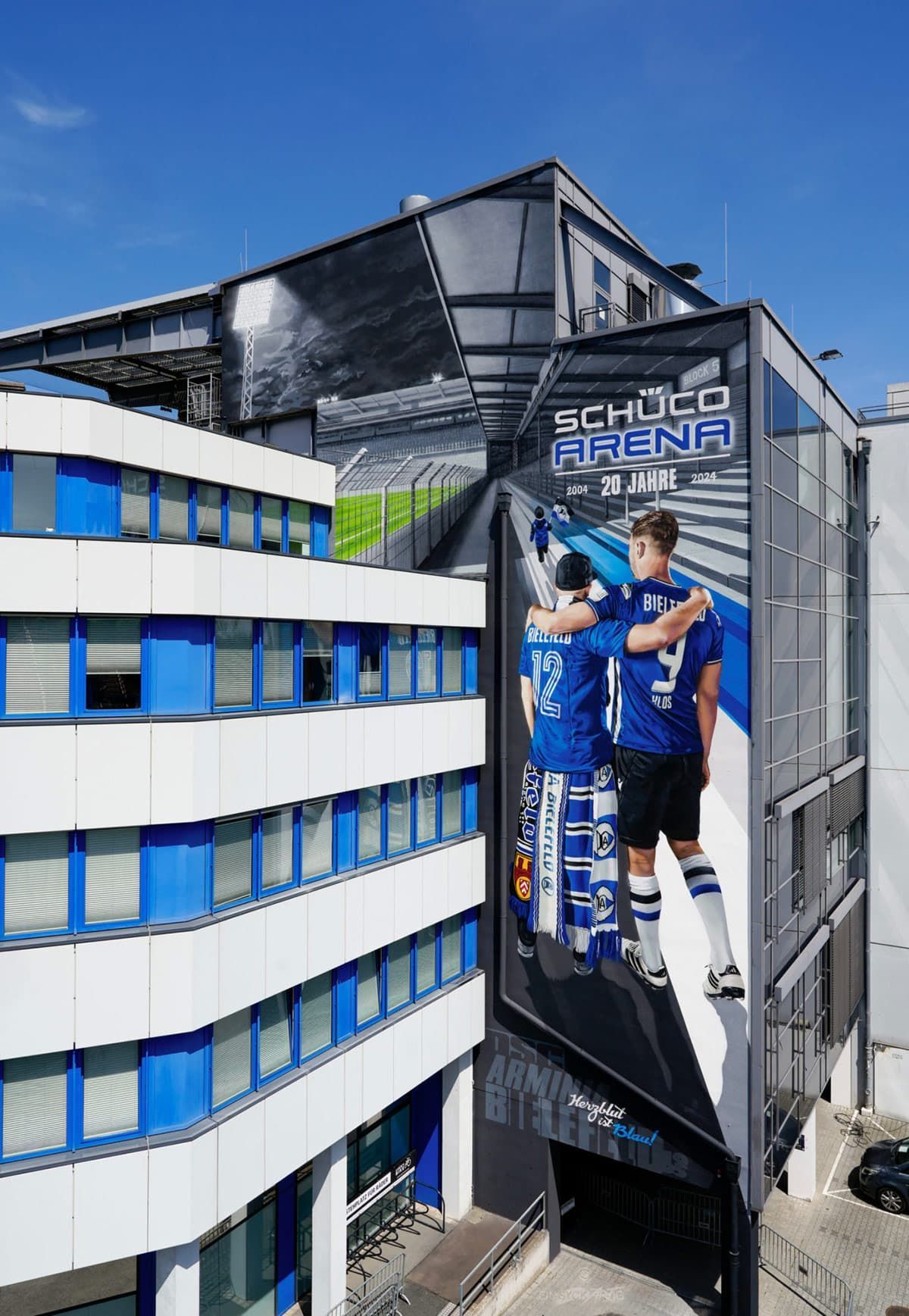 Großformatige Wandgestaltung an der SchücoArena Bielefeld, komplett mit Graffiti-Sprühdosen gemalt; fotorealistische Darstellung von Fan und Fabian Klos vor Stadionkulisse zum 20-jährigen Jubiläum.
