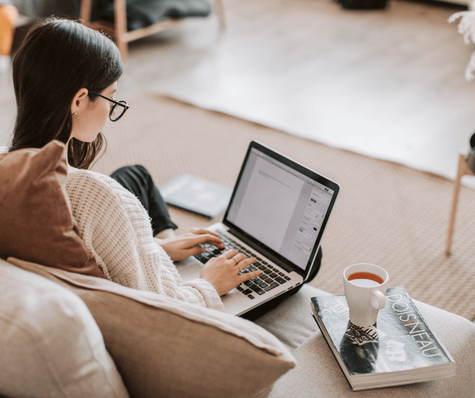 Person working on a laptop from the sofa with a coffee – remote admin or application form