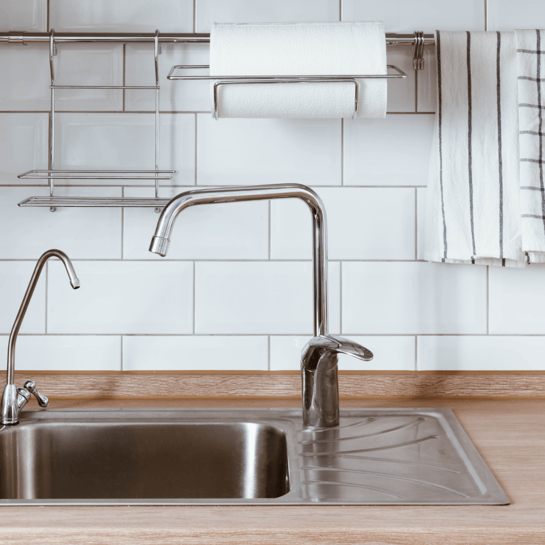 Shiny chrome kitchen tap and sink in front of white tiled splashback – deep kitchen clean