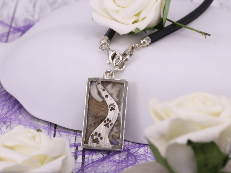 rechteckiger Kettenanhänger mit eingefassten Zähnen und Hundehaaren, das Design erinnert an einen Weg mit Pfotenabdrücken