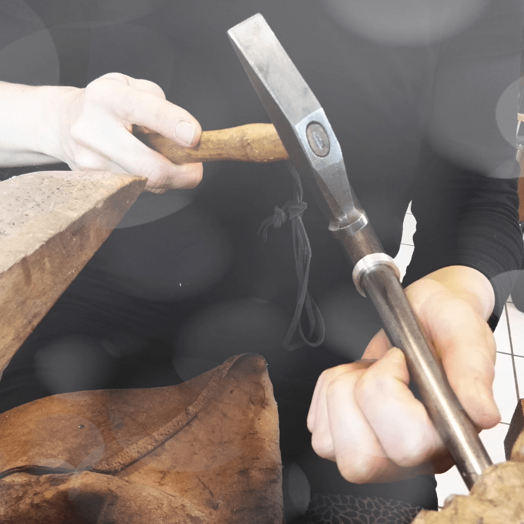 Blick auf eine Goldschmiedin, die gerade einen Ring auf dem Ringriegel mit einem Hammer schmiedet