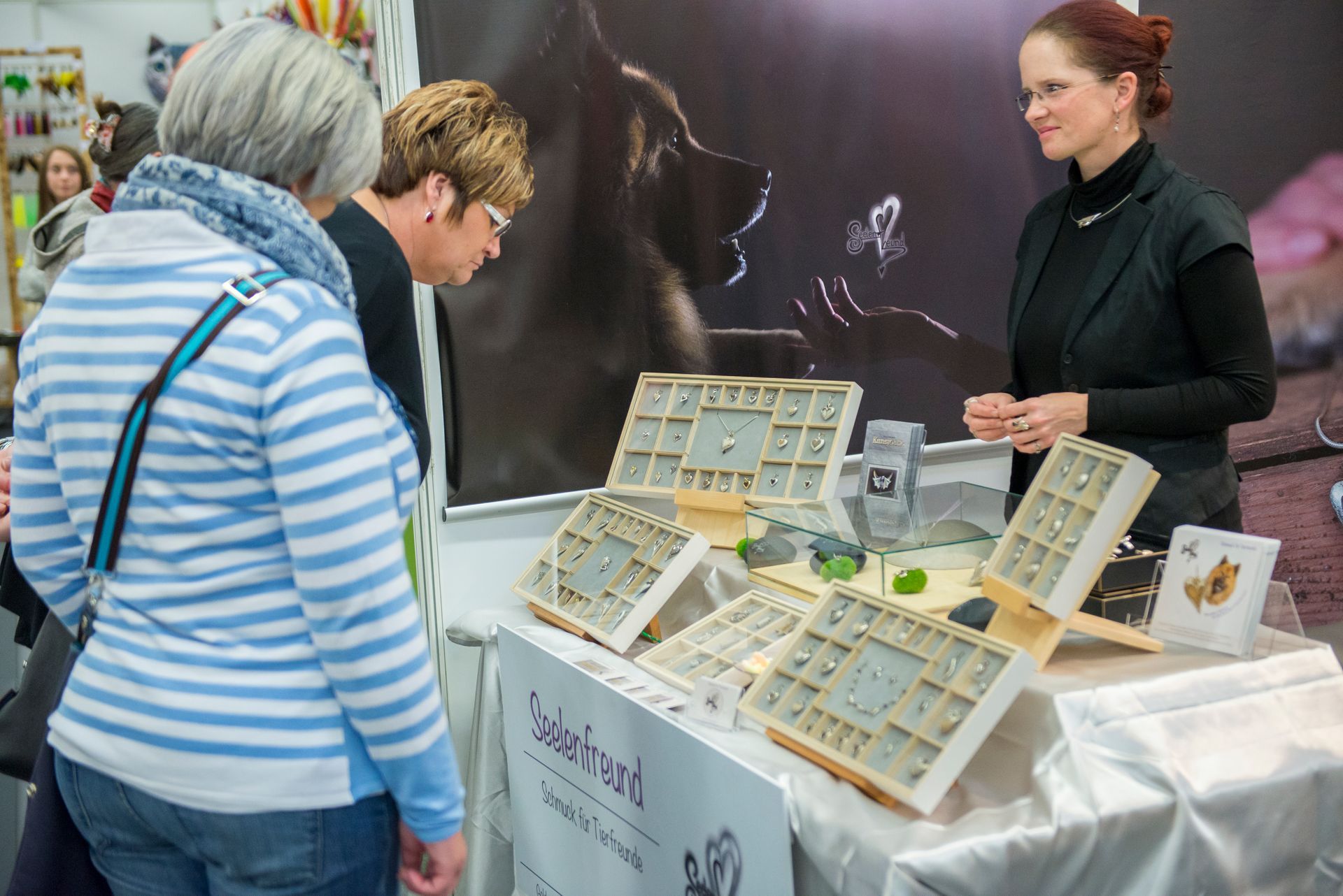 Zwei Besucherinnen der Heimtiermesse lassen sich die verschiedenen Modelle zeigen und erfahren wichtige Kriterien für die Einarbeitung der Haare in die Schmuckstücke.
Am Messestand können die Schmuckstücke genau betrachtet werden und die Kunden können sich von der guten Qualität und der angenehmen zu tragenden Haptik überzeugen.
