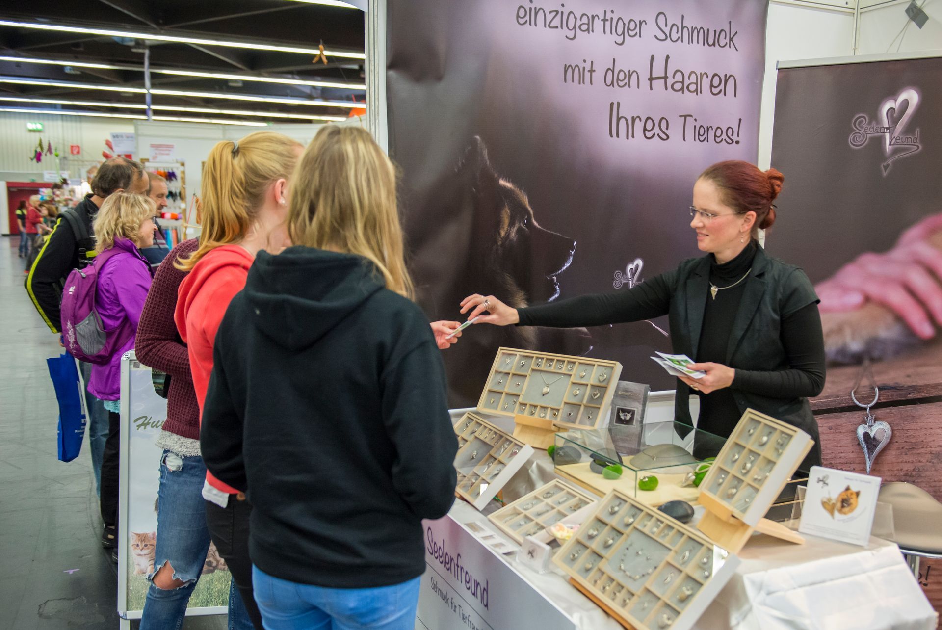 Goldschmiedin Elke Wagner aus Heroldsberg gibt zwei Besucherinnen der Consumenta in Nürnberg Infomaterial über den Schmuck von Seelenfreund.
Beide Damen haben eien Hund und möchten sich in ein Schmuckstück die Haare des eigenen Tieres einarbeiten lassen.
Genau für solche Momente ist der Messe sinnvoll und eine große Bereicherung