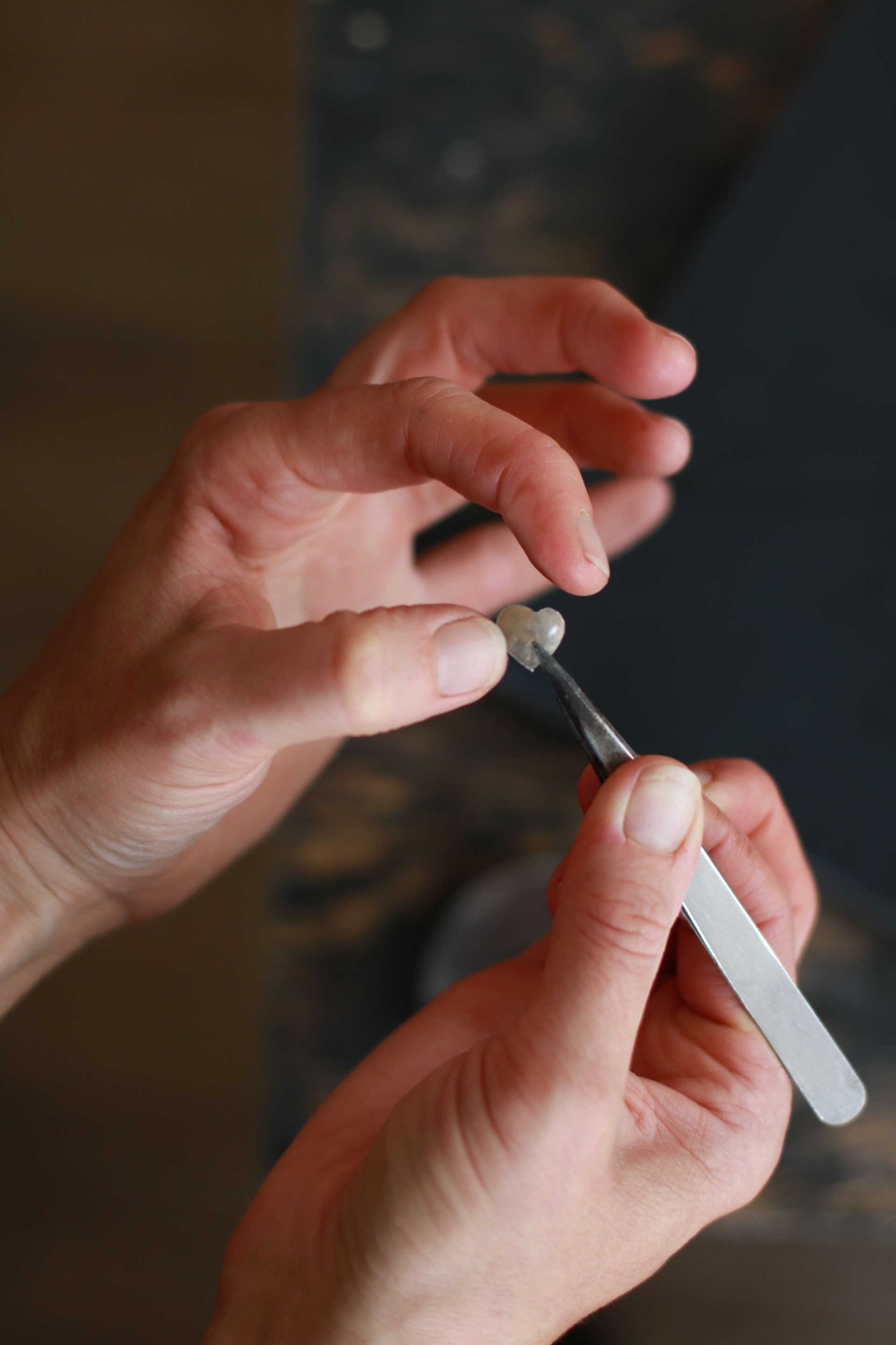 Zwei Hände, die eine umfasst eine Pinzette, die andere umgreift ein kleines Herz aus Gold