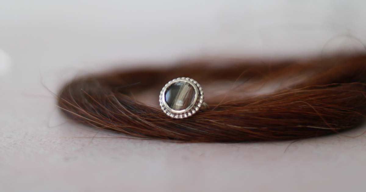 Ring aus Silber mit eingefassten Pferdehaaren Ring aus Silber mit verspieltem Fassungsrand und eingefassten Pferdehaaren, Der Ring liegt auf einer dicken Strähne aus Pferdehaaren.