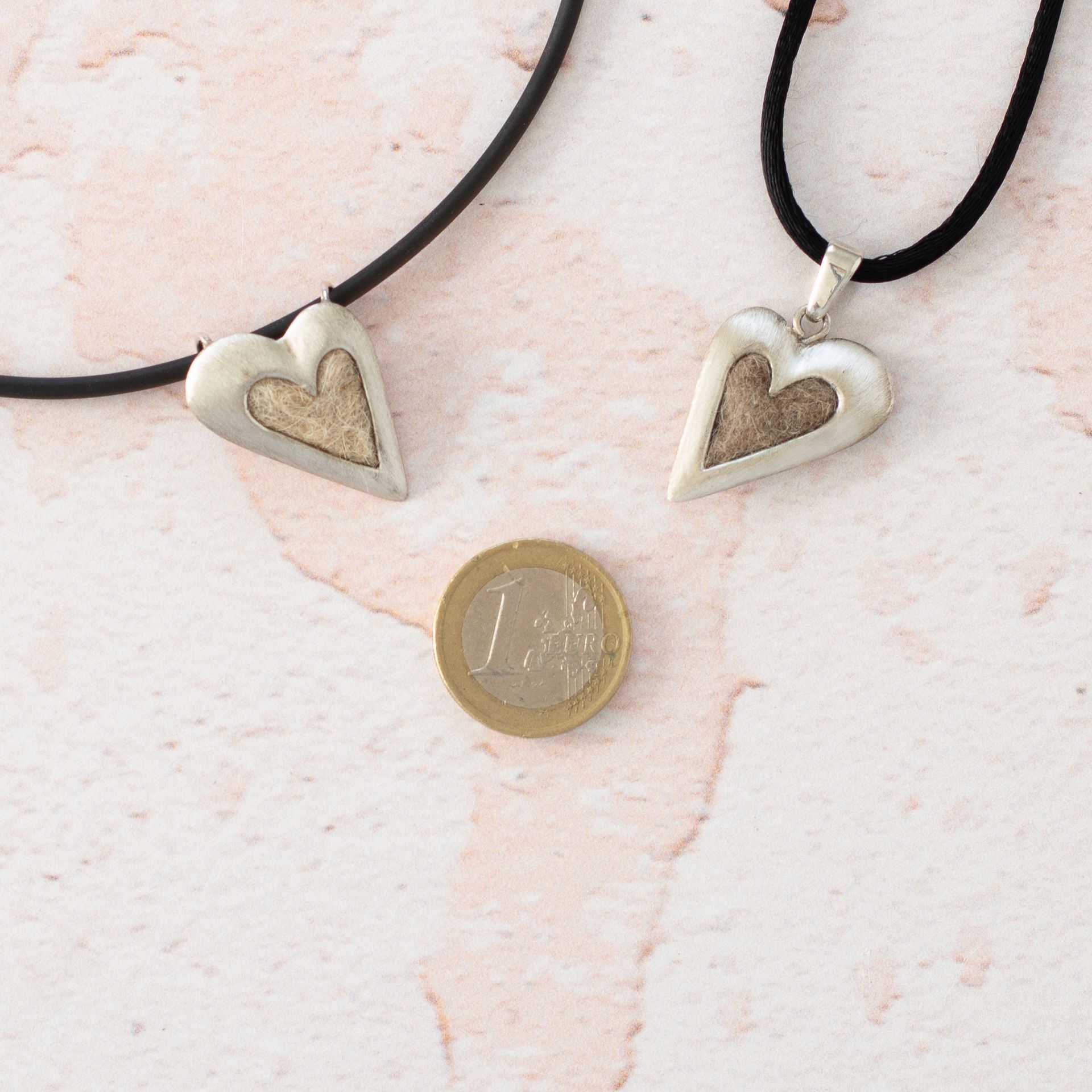 zwei herzförmige Kettenanhänger mit eingefilzten Tierhaaren neben einer 1 euro Münze