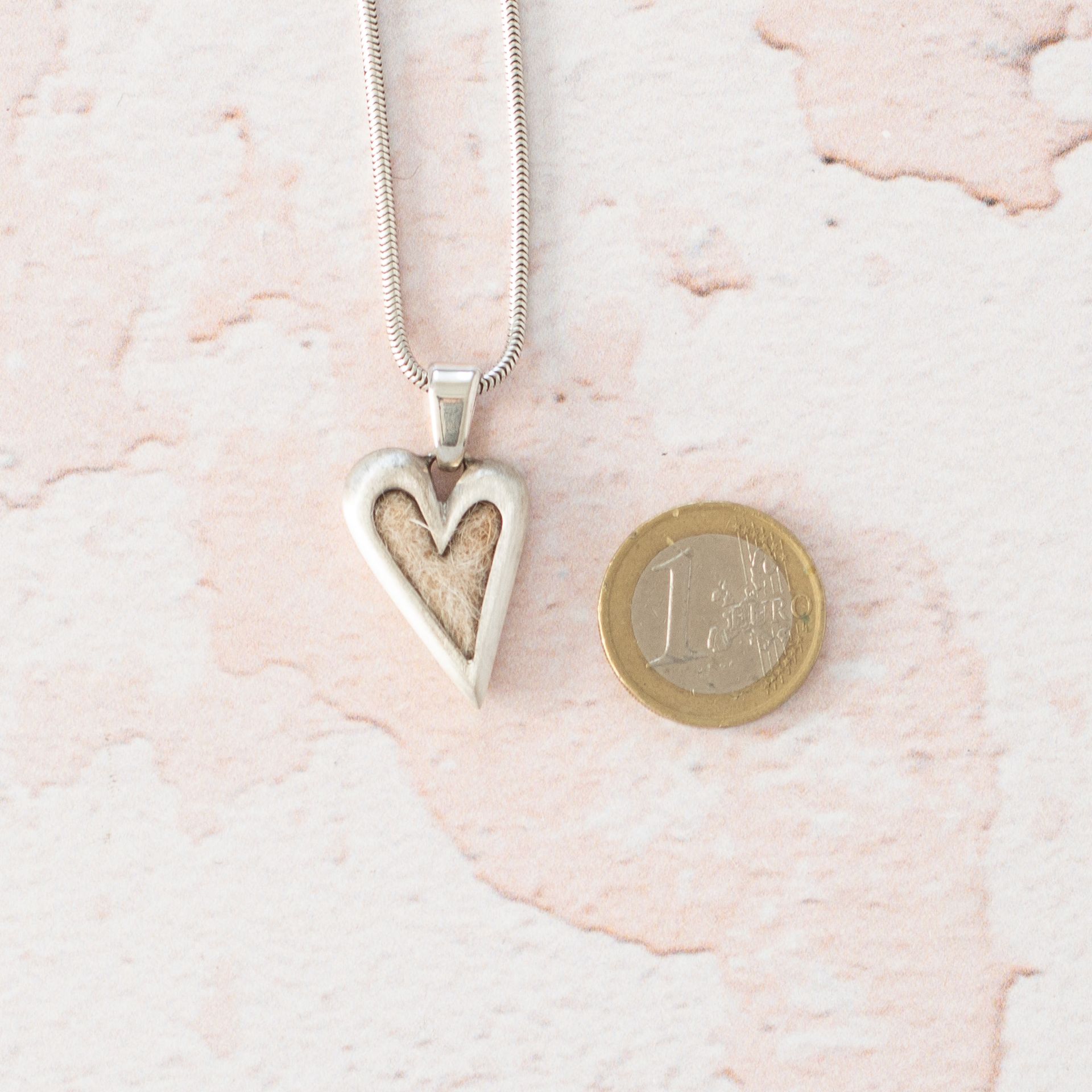 Kettenanhänger in Herzform mit eingearbeiteten Tierhaaren Schmuck mit Tierhaaren von Seelenfreund. Das Modell Soulfriend mit eingefilzten Hundehaaren neben einer 1 Euro Münze