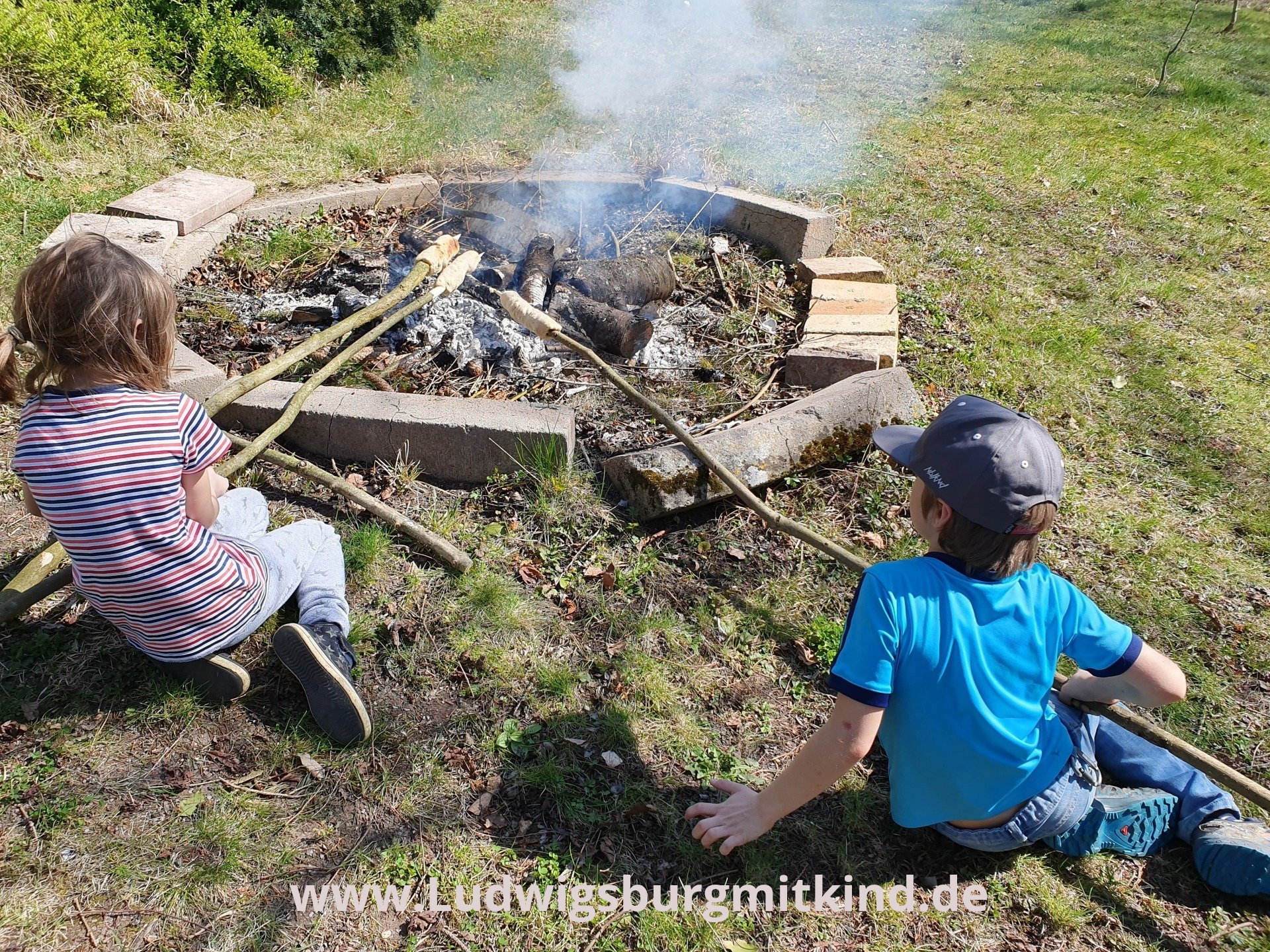 Zwei Kinder grillen Stockbrot über einem Lagerfeuer.