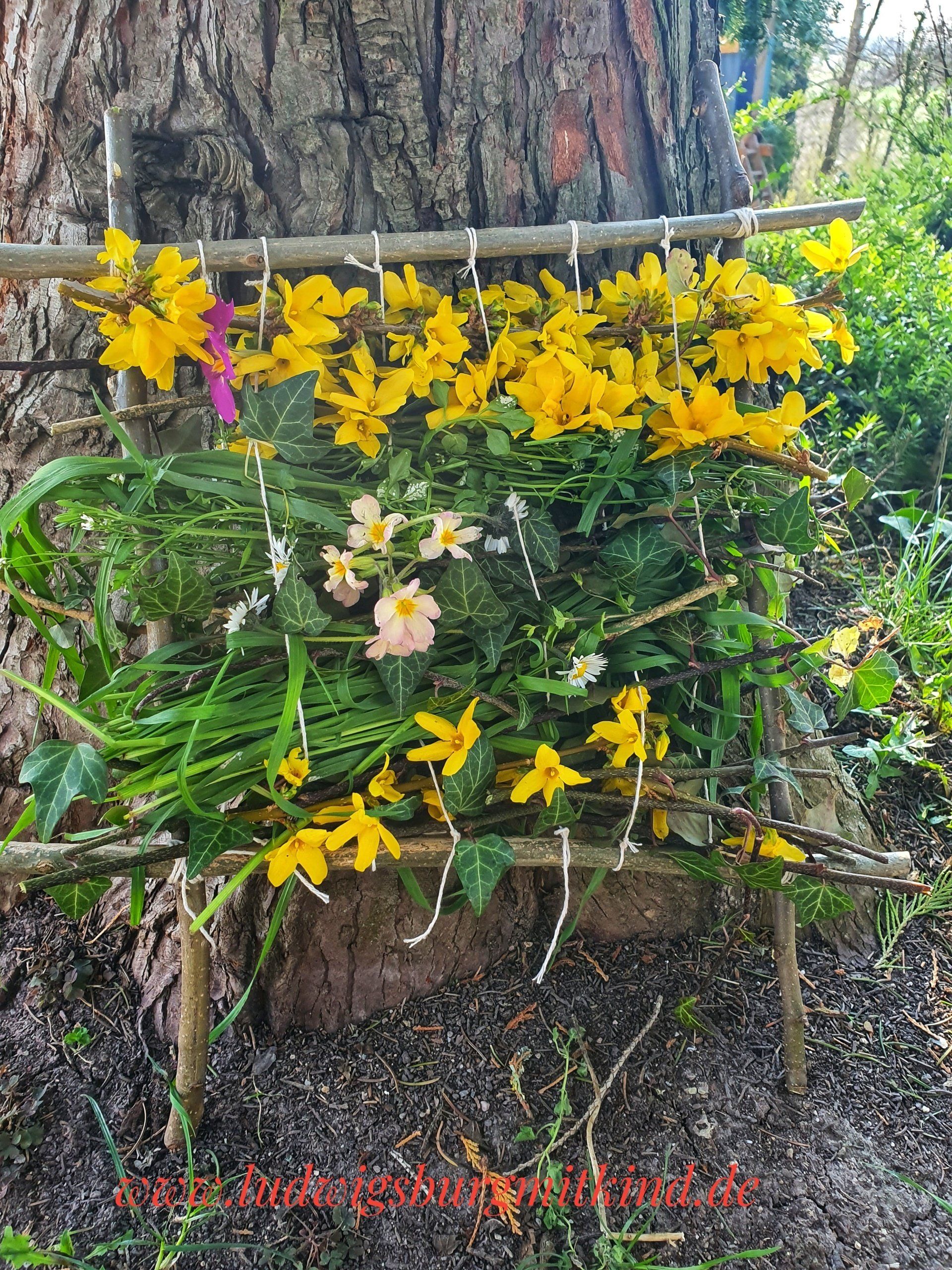 Ein Webrahmen aus Haselzweigen mit Blumen verwebt.