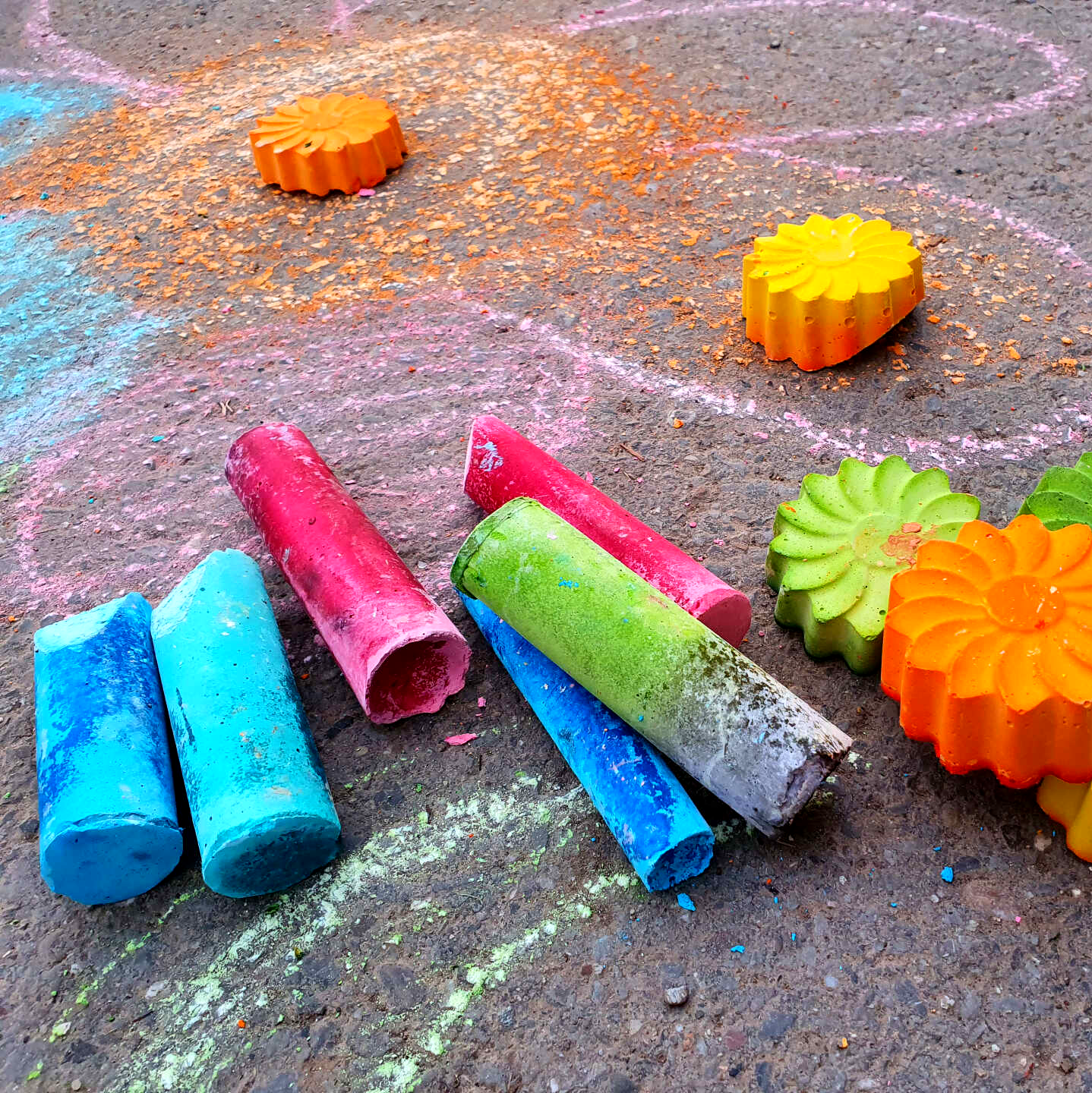 Selbst gemachte Straßenkreide in Blumenform liegt auf einer Straße. Kinder malten damit eine Bume