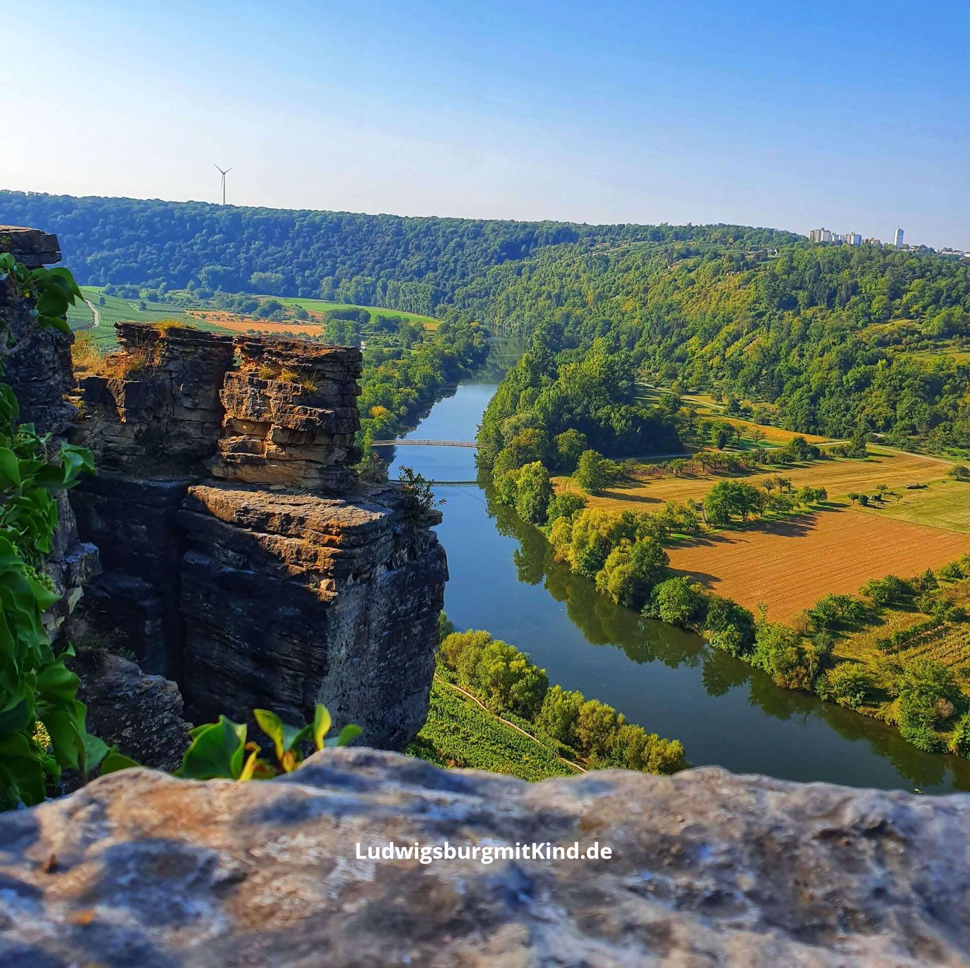 Kind sitzt bei einer Familienwanderung auf den Hessigheimer Felsengärten mit Blick auf den Neckar und die Weinberge.