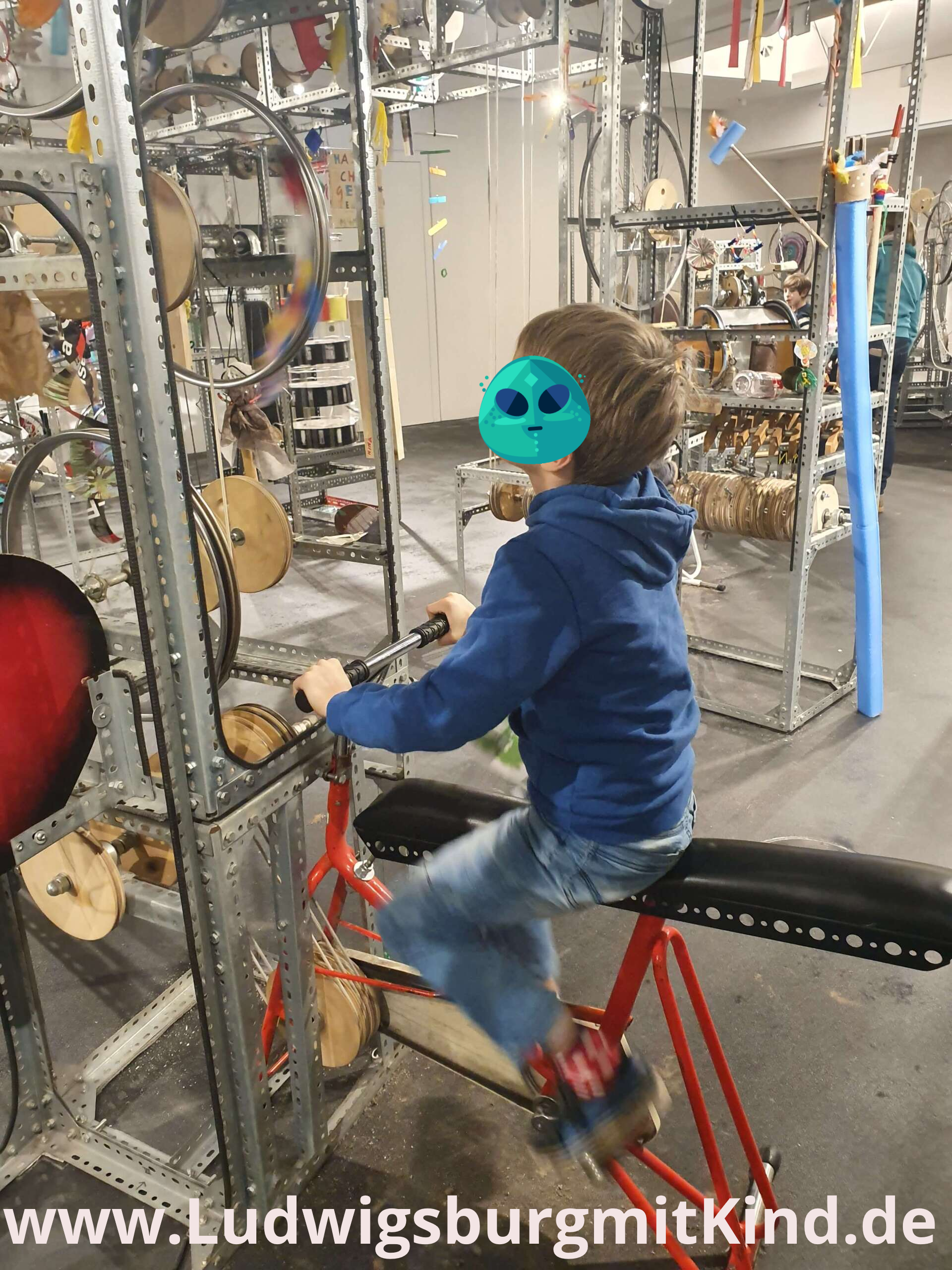 Ein Kind sitzt auf einem Fahrrad in der Mitmachmaschine im Kindermuseum Ludwigsburg und treibt so viele Räder an.