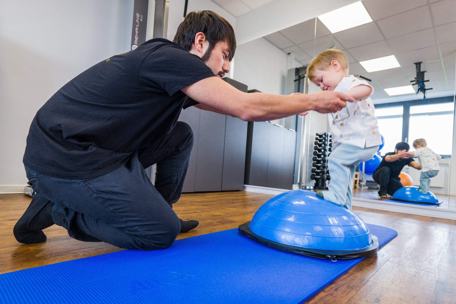 Ein Physiotherapeut hilft einem Kind beim Stehen auf einem Ball.