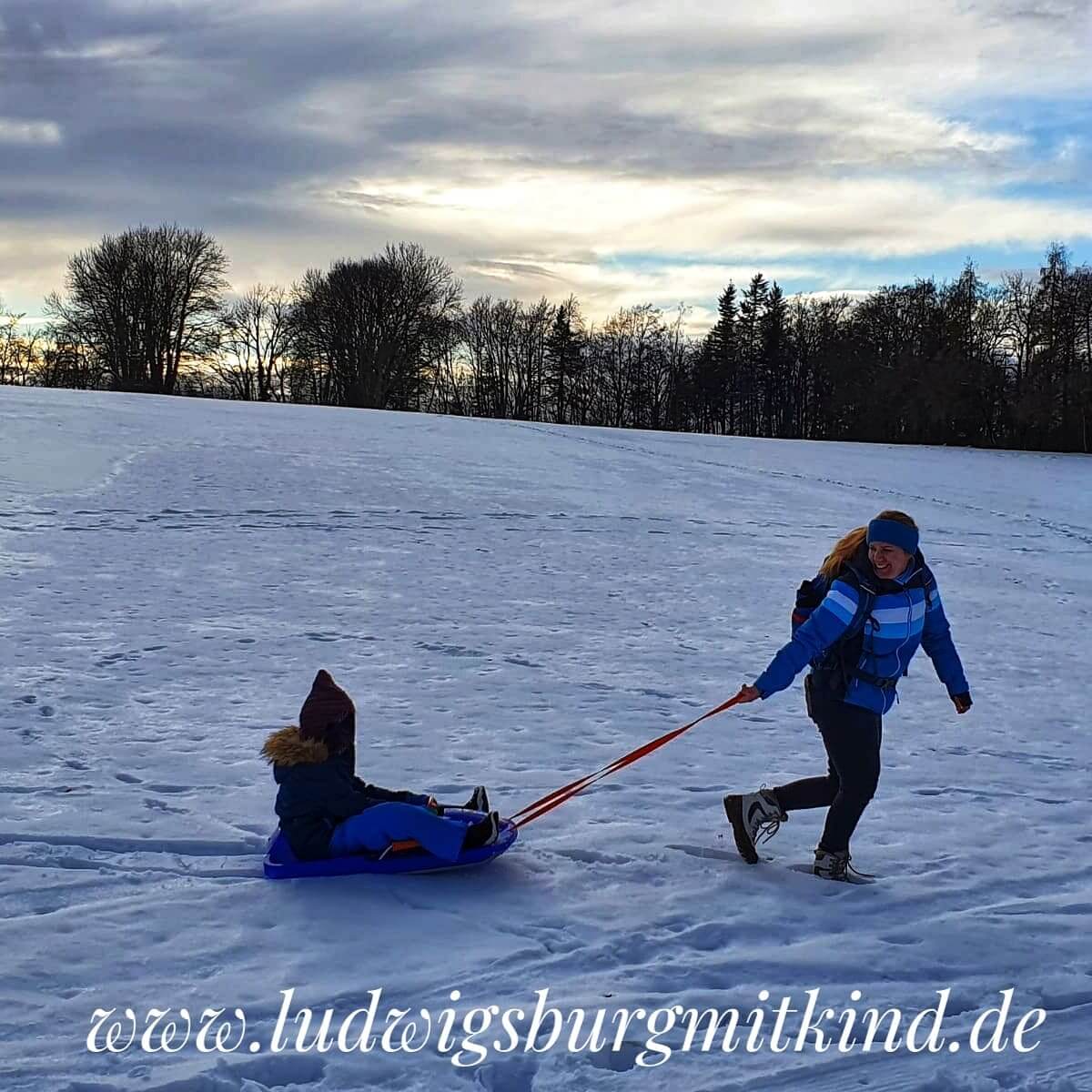 Eine Mutter zieht ihr Kind auf einem Schlitten im Schwarzwald