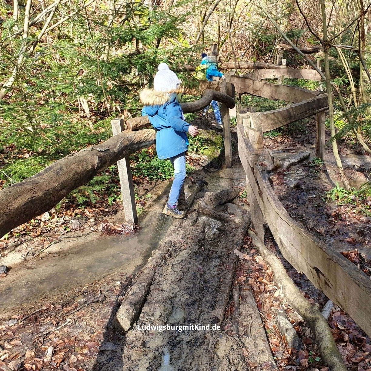Kinder balancieren auf einem Balken im Matsch des Walderlebnispfades Sinneswandel für Kinder in Bad Boll auf der Schwäbischen Alb