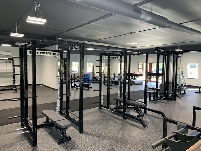 wide shot of multiple squat racks, bench press benches, and a monolift