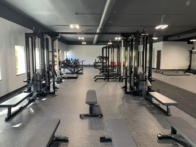 Wide shot of cable machines with other weightlifting equipment in the background deadlit platform and benches