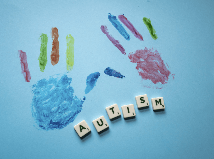 Scrabble letter spelling the word 'autism' with child's painted handprints above it