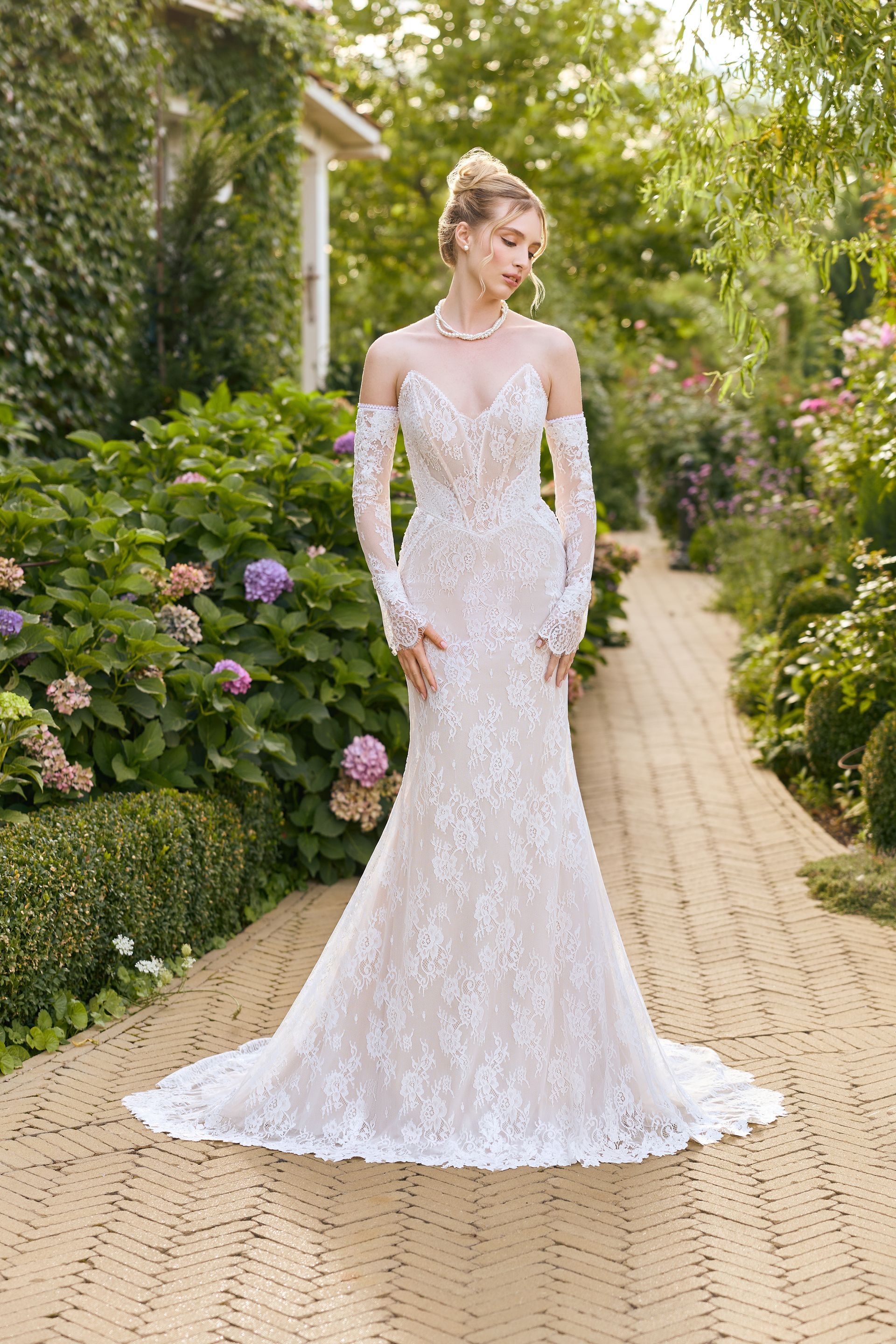 Das Brautkleid auf dem Bild erhältst du bei Amorely Brautmoden RUHRGEBIET. Eine junge Braut trägt ein elegantes Fit & Flare-Brautkleid mit v-förmiger Corsage, Herzausschnitt und Lingerie-Effekt. Das Kleid ist aus feiner französischer Spitze gearbeitet und hat abnehmbare Spitzenärmel. Der figurbetonte Schnitt betont die Silhouette und verleiht dem Look eine romantische Note.