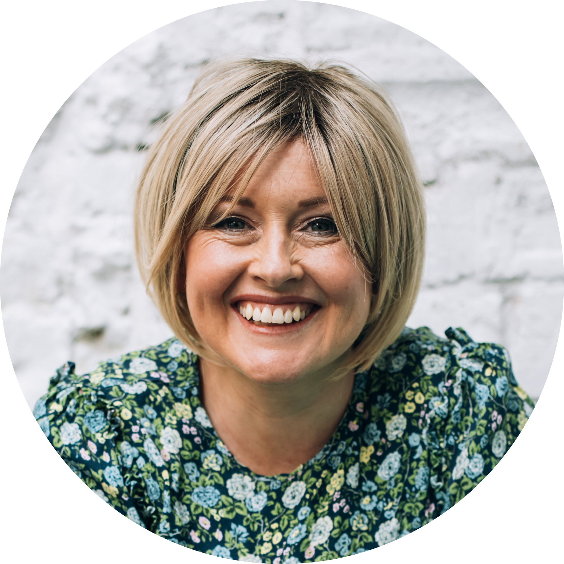 Headshot of Jenn smiling with a white brick wall behind her.