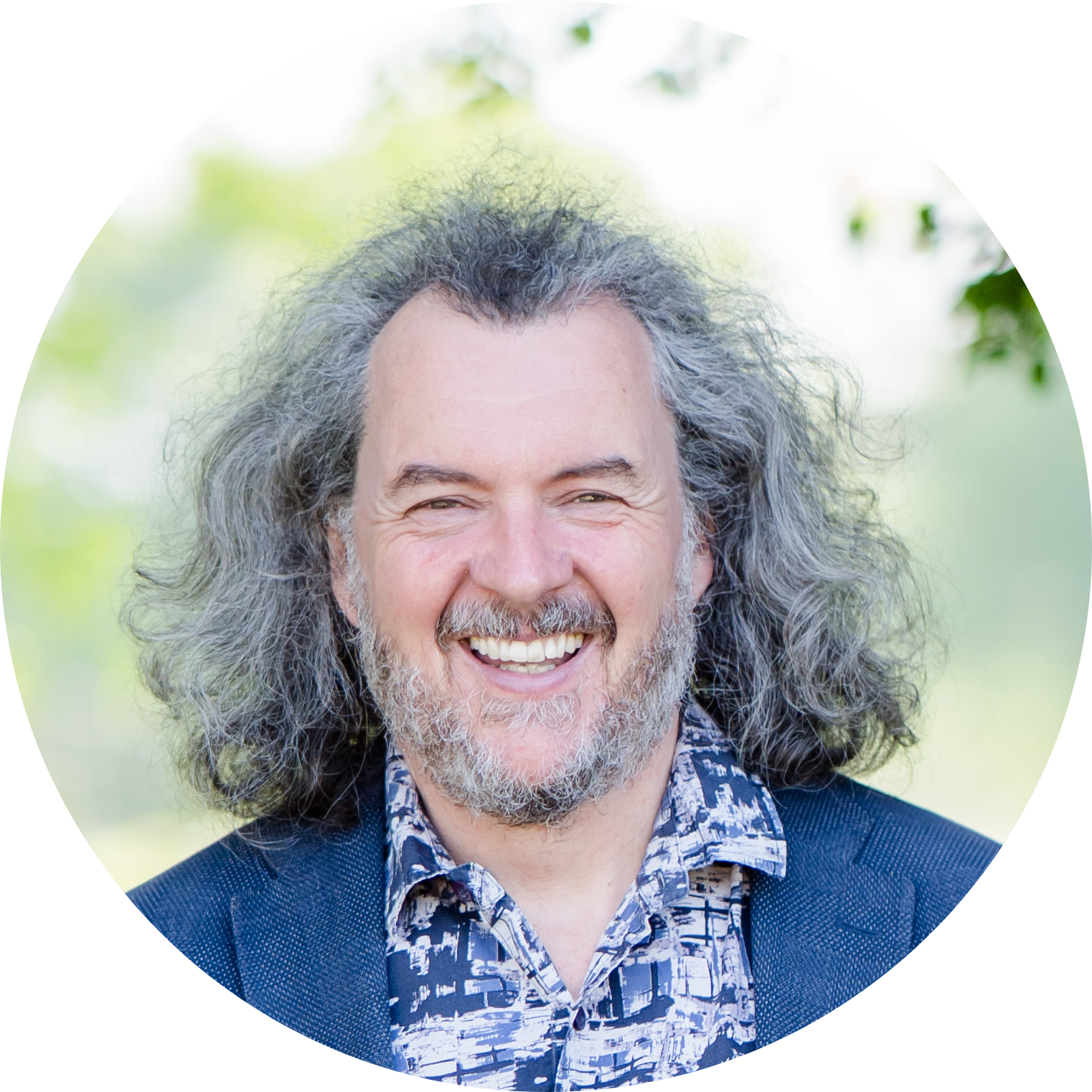 Headshot of Nic smiling outdoors with greenery in the background.