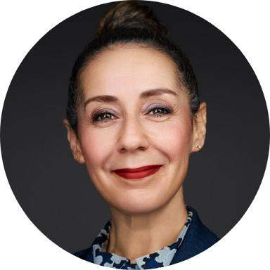 Headshot of Soulaima beaming, against a dark background. Her dark brown hair is in a topknot and she's wearing a deep red lipstick.