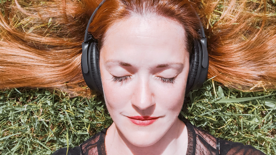 Femme détendue écoutant un audio d’hypnose sur son canapé, symbole de bien-être accessible partout