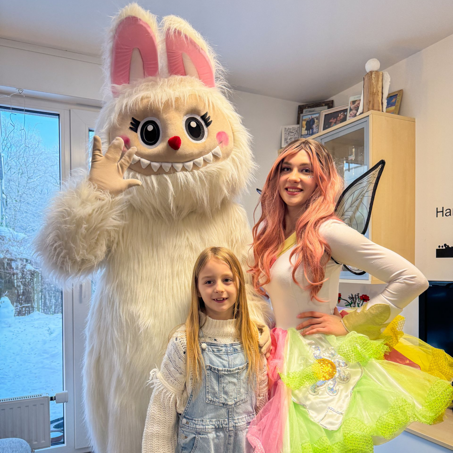 ein Kind steht lachend zwischen einem Labubu-Maskottchen und einer Fee