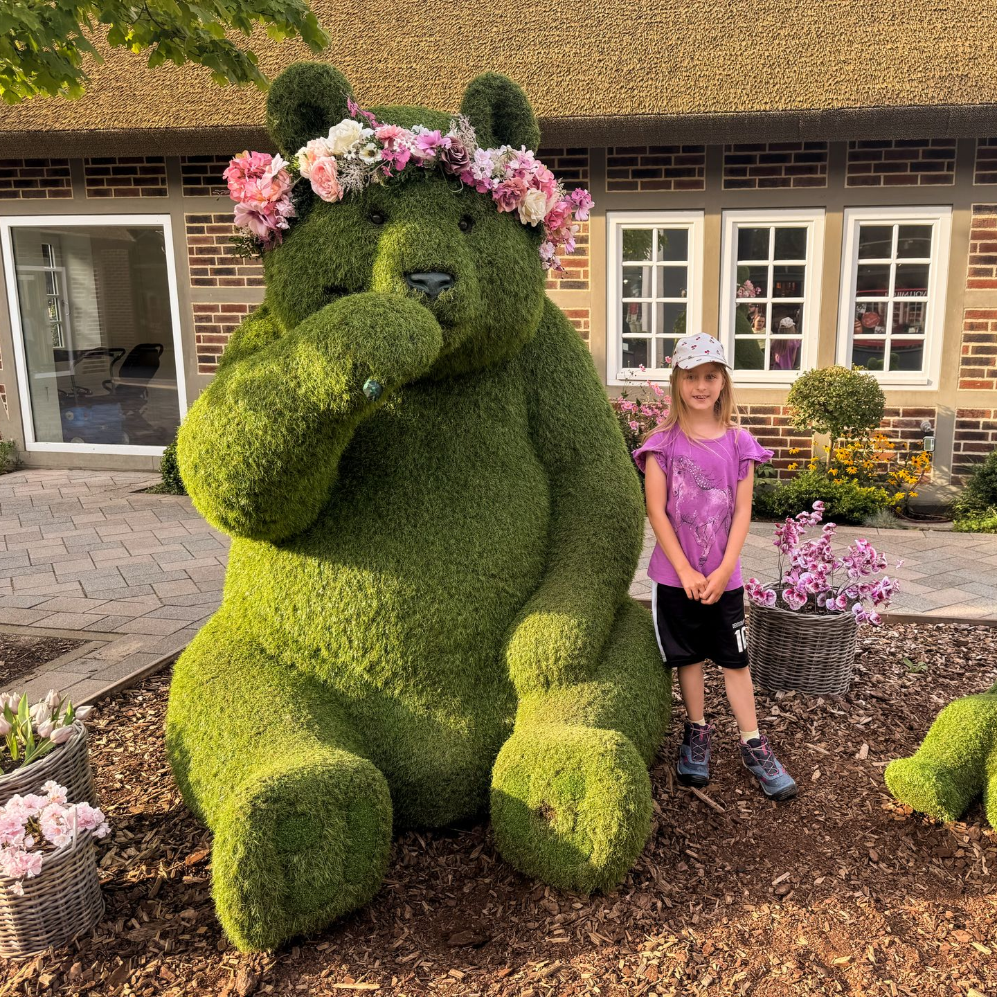 Mädchen steht neben einem großen Teddy aus Gras