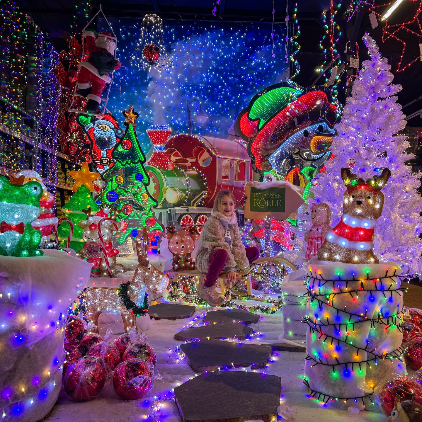 Hamburg mit Kind Pflanzen-Kölle Gartencenter Kind sitzt zwischen leuchtender und glitzernder Weihnachtsbeleuchtung