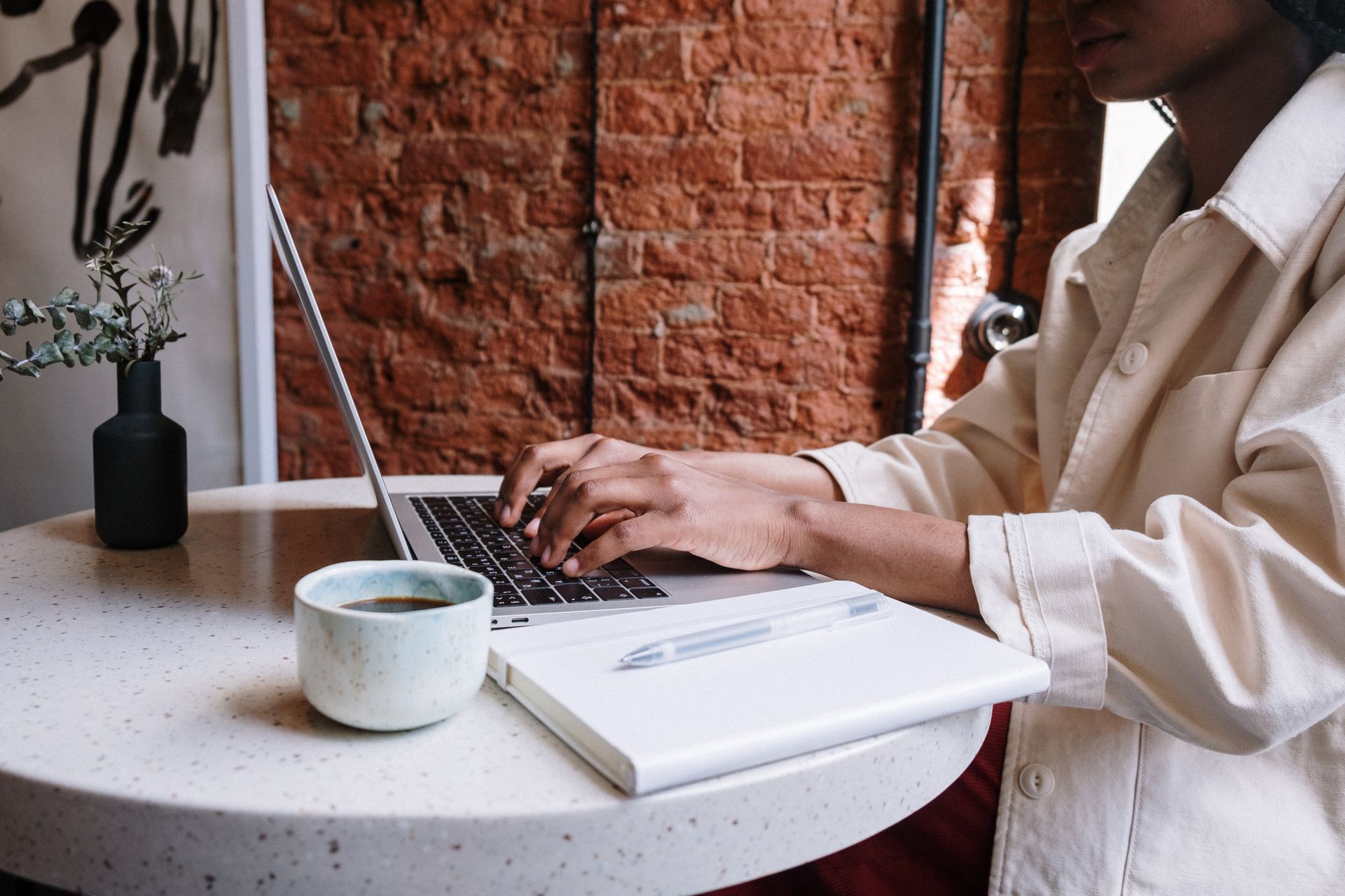 Black woman wearing white shacket typing on laptop, sitting at small round table