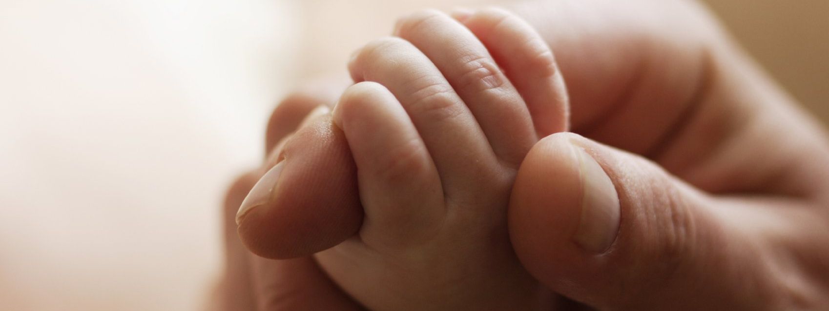 Hand of a father holding the foot of a child whose paternity he rejects