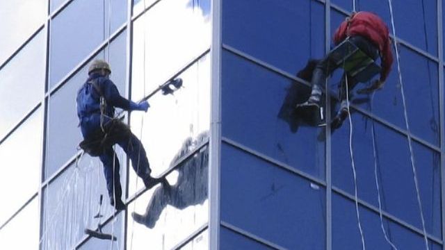 Versicherung für Immobilie im Bau in Italien Zwei Fensterputzer arbeiten gemäß Immobilienbaurecht Italien an der Außenseite eines Hochhauses, das über eine Versicherung für Immobilie im Bau in Italien verfügt.