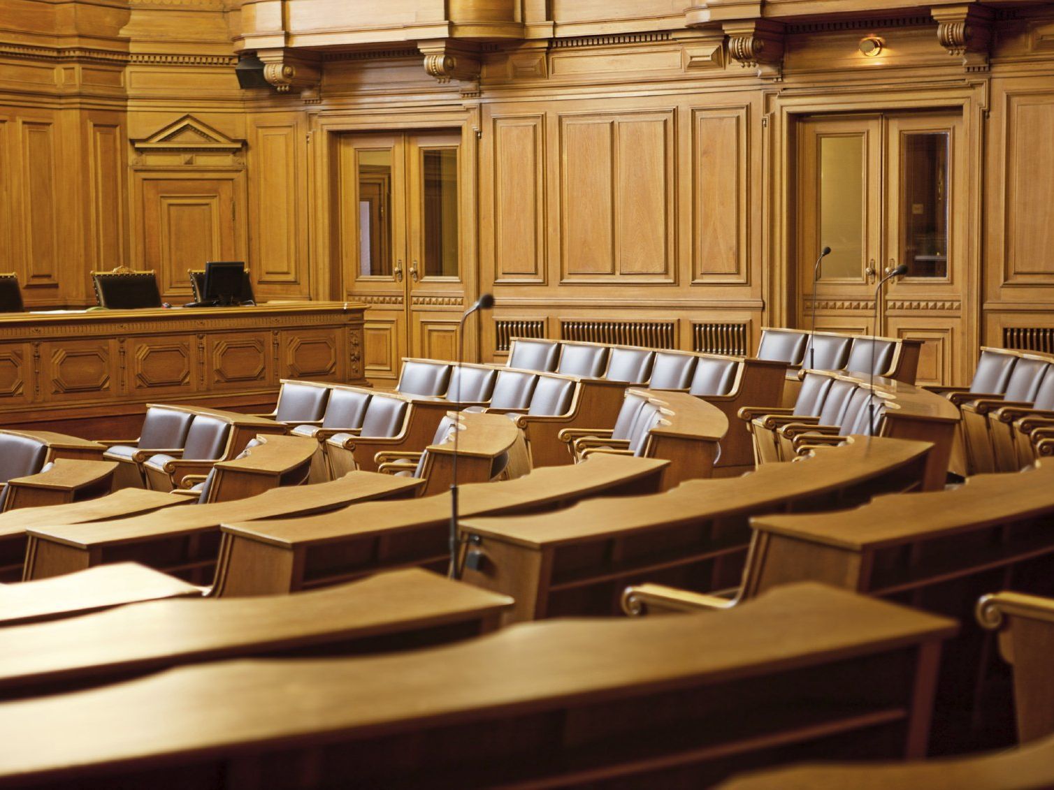 Ein leerer, holzgetäfelter Gerichtssaal mit Reihen von Bänken und Schreibtischen, bereit für eine Sitzung zur Italienischen Mediation.