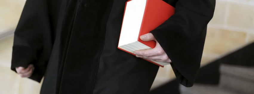 Ein Richter in einer schwarzen Robe, die ein rotes Buch über italienisches Prozessrecht zum Forderungseinzug unter dem Arm trägt.