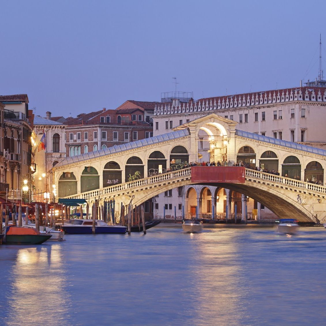 The Rialto Bridge, illuminated at dusk by boats on the Grand Canal in Venice, Italy, reflects the latest developments in Italian law