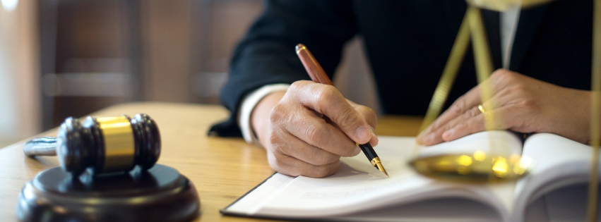 Ein italienischer Anwalt, die an einem Schreibtisch in eine Mahnung schreibt. Ein Hammer und eine Waage der Gerechtigkeit sind sichtbar und symbolisieren den Forderungseinzug in Italien