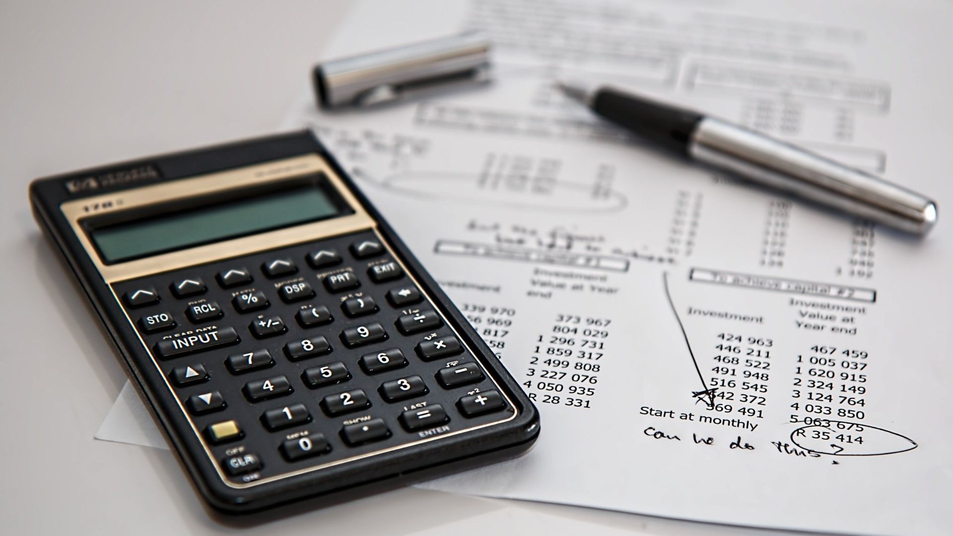 A calculator, a pen and financial documents on a desk showing calculations or budget planning for a guarantee for property under construction in Italy.