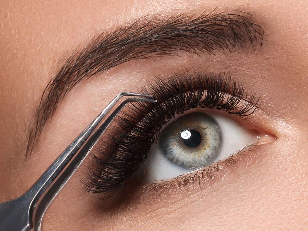 Detailaufnahme eines Auges während einer Wimpernverlängerung mit Pinzette.