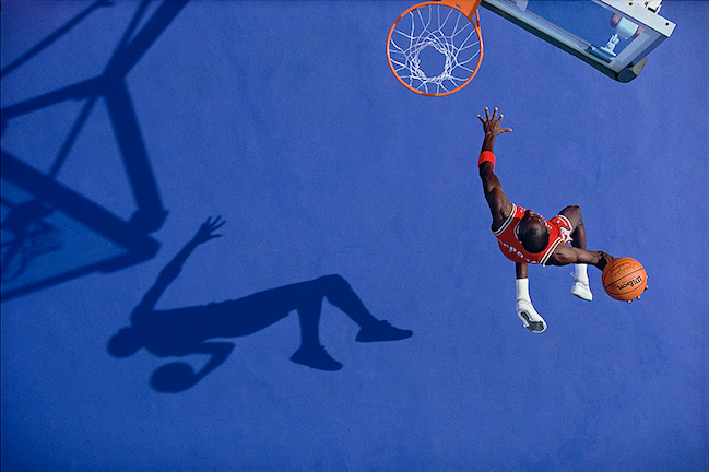 A bird's eye view action shot of professional
basketball athlete Michael Jordan mid-air on the way to
dunking a basketball in a nearby hoop.