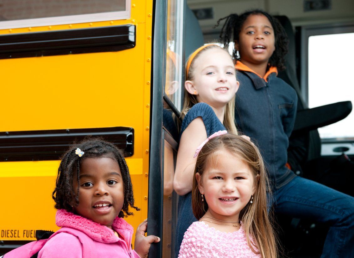 Four smiling girls, on and next to a yellow school bus.
