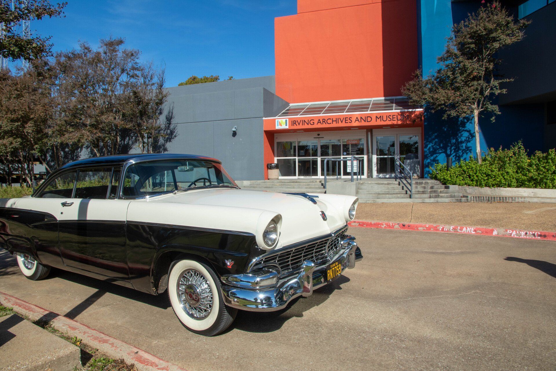 A black and white vintage car in front of the Irving Archives and Museum under a blue sky.
