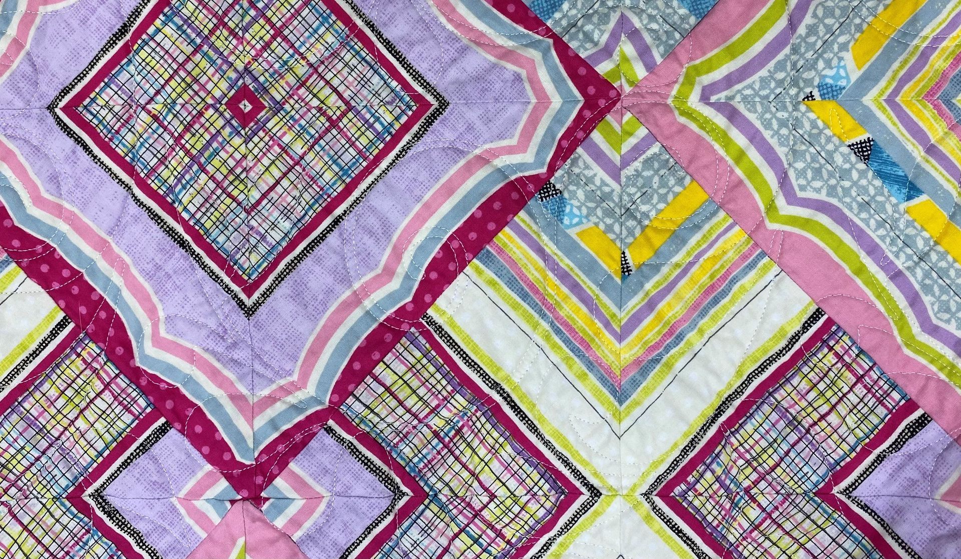 Vibrant geometric quilt with squares and chevrons in purple, pink, yellow, blue, and green.