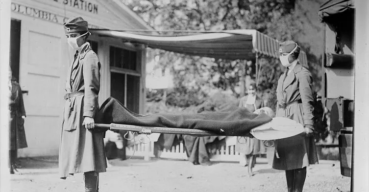 Nurses in masks and uniforms carry a masked patient on a stretcher to an ambulance station.