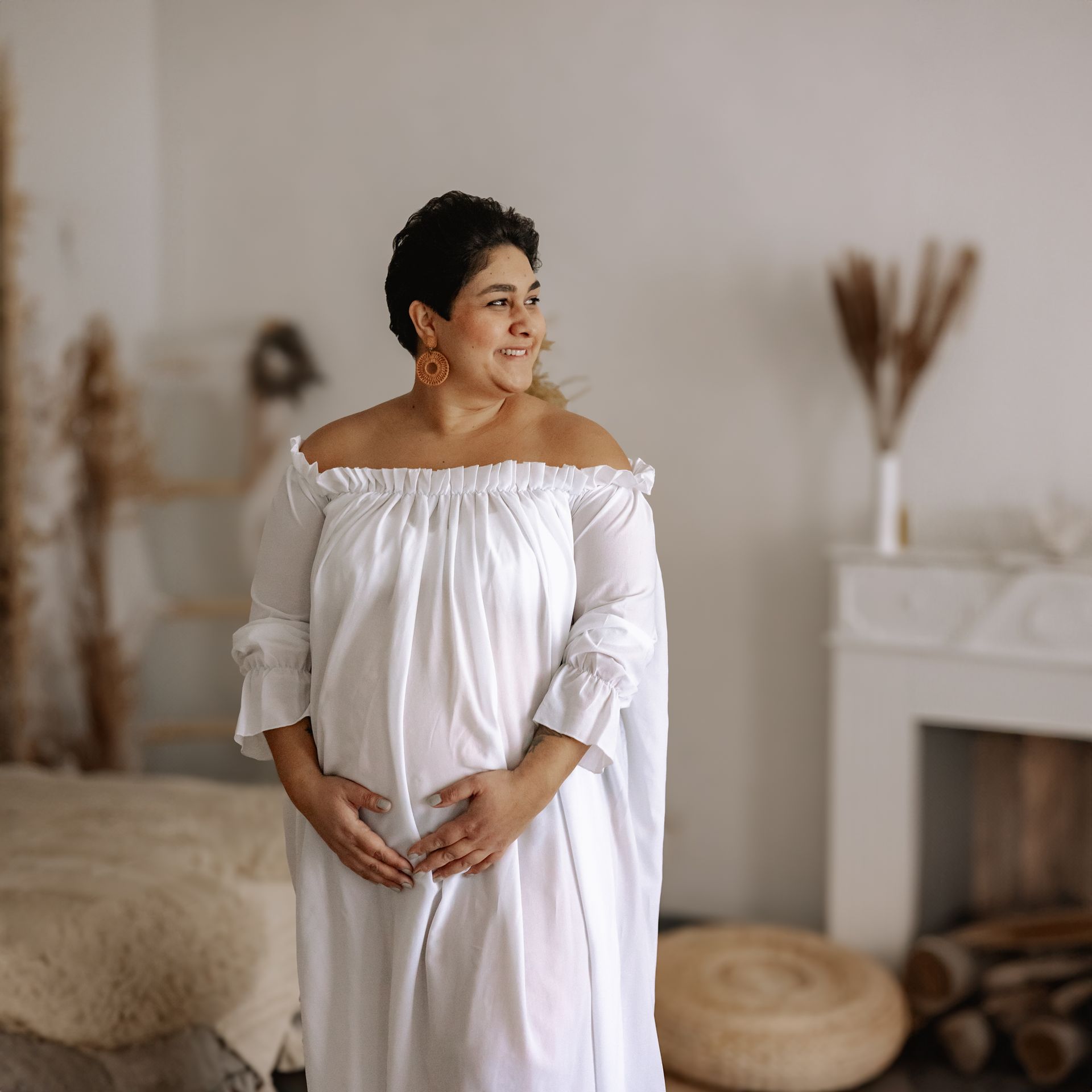 Schwangere Frau im weißen Babybauchkleid vor Kamin in meinem Babyfotostudio