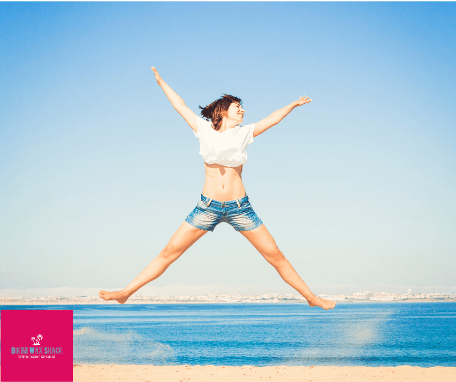 Lady on a beach mid star jump. Bikini Wax Shack logo.