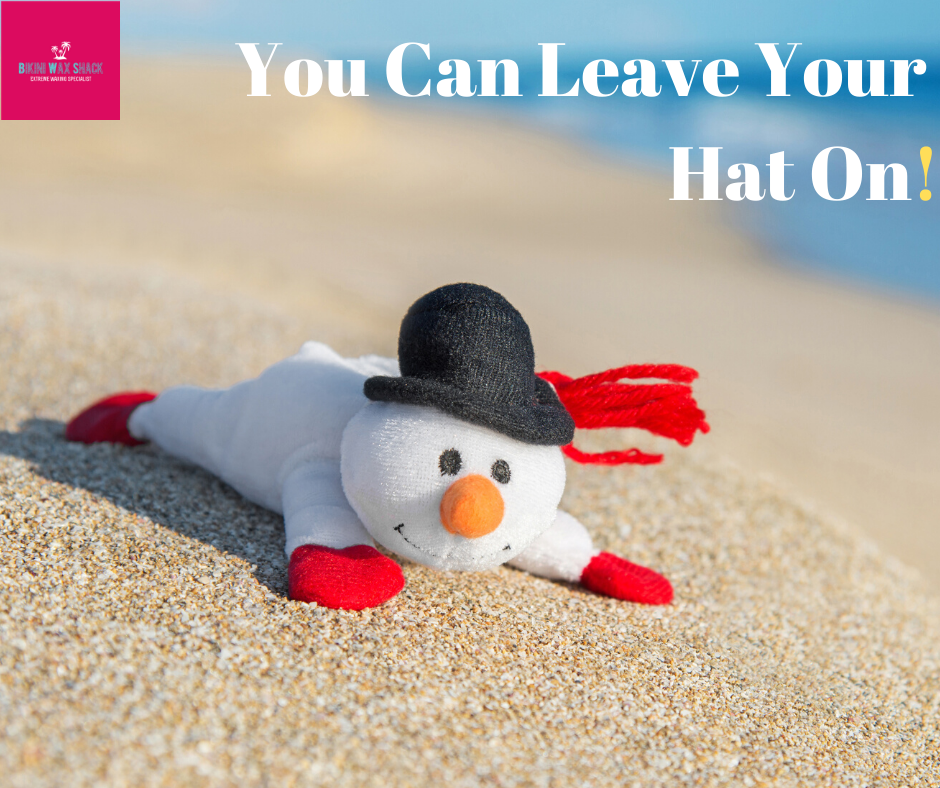 Sand snowman laying down on the beach. slogan reads you can leave your hat on!